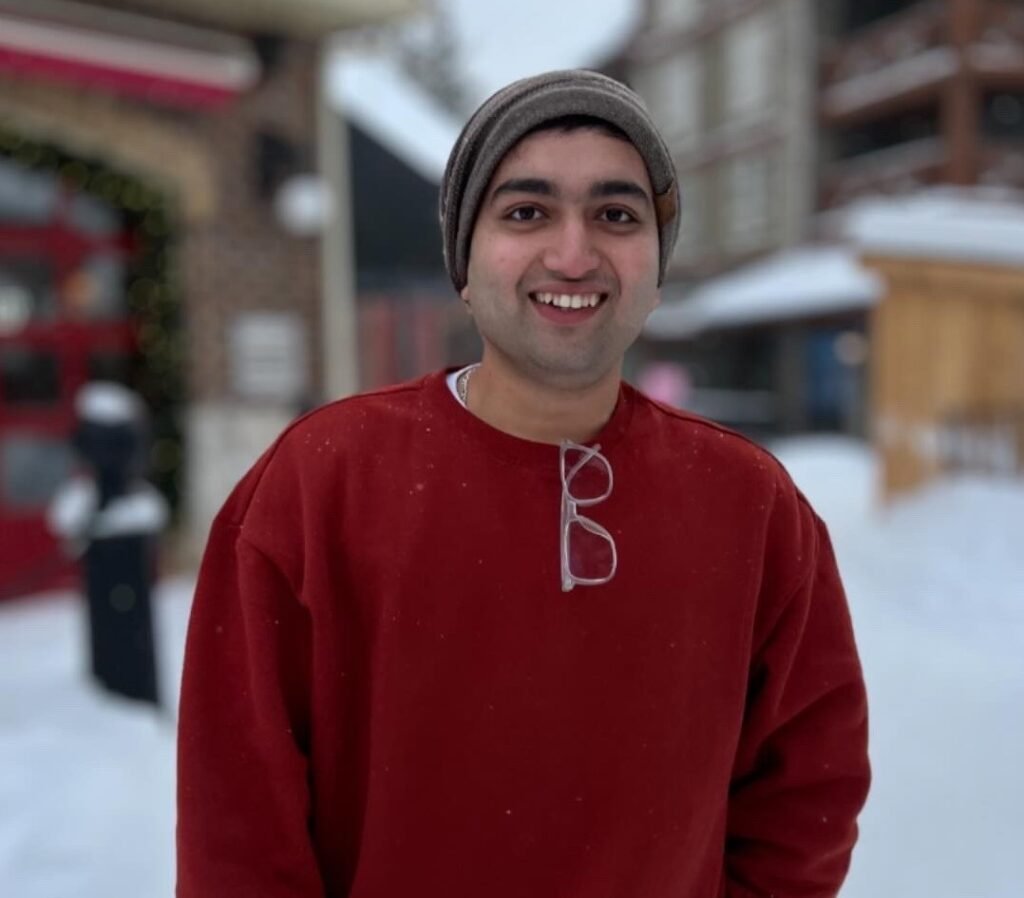 Rushabh Kakodkar smiling outdoors in a red sweater, standing in a snowy background, radiating a friendly and warm presence.